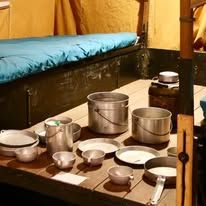 Historic RV interior display featuring metal cookware, plates, and utensils